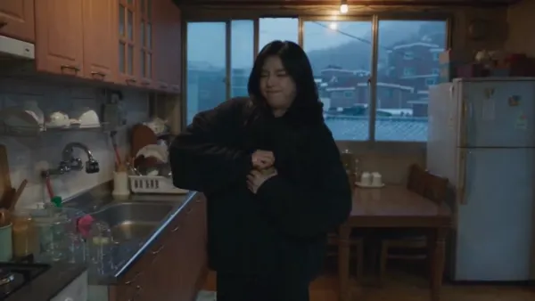 어두운 비 오는 밤, 서울 낡은 아파트 작은 주방에 있는 오버사이즈 티셔츠 차림의 젊은 한국 여성